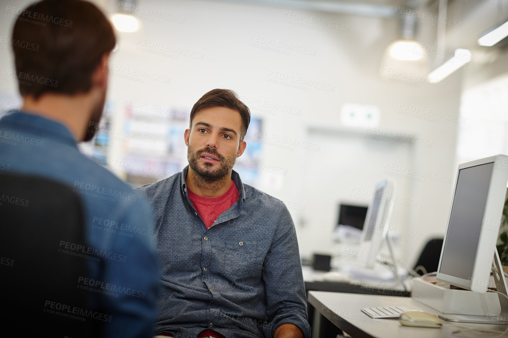 Buy stock photo Shot of two young businessmen talking together at a desk in an office