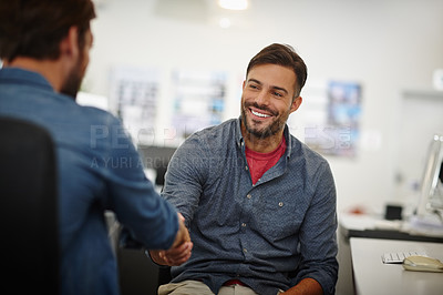 Buy stock photo Shot of two young businessmen shaking hands together at a desk in an office