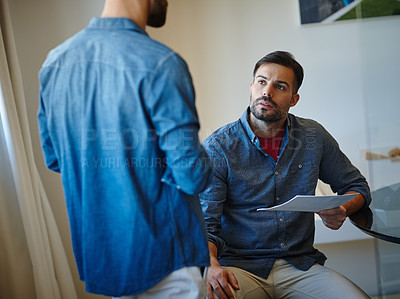 Buy stock photo Shot of two young businessmen talking together at a desk in an office