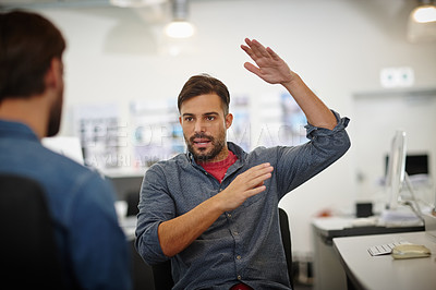 Buy stock photo Shot of a young businessman gesturing while explaining something to his colleague in the office