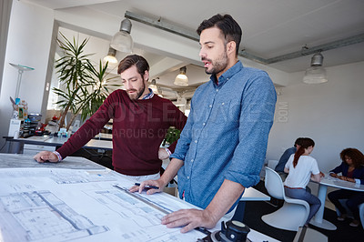 Buy stock photo Shot of two architects looking at blueprints together in their office