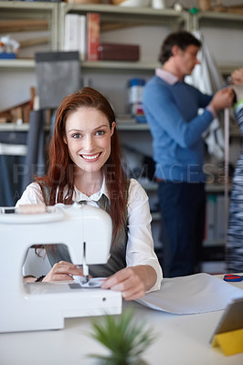 Buy stock photo Portrait of a young fashion designer sewing while a colleague works in the background
