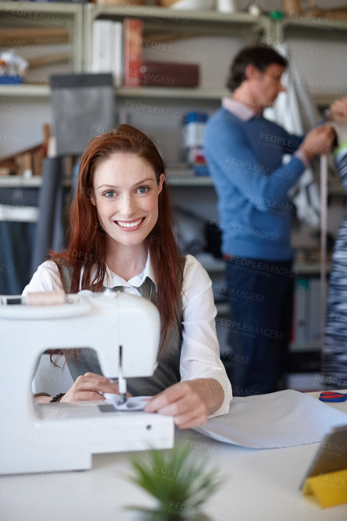 Buy stock photo Portrait of a young fashion designer sewing while a colleague works in the background