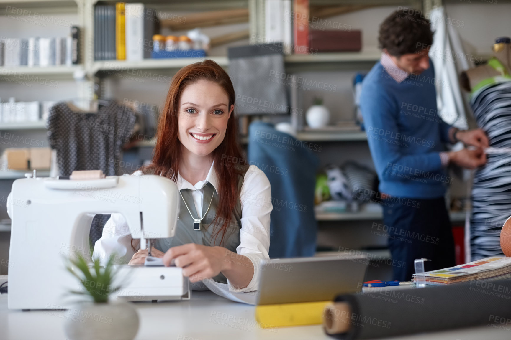 Buy stock photo Portrait of a young fashion designer sewing while a colleague works in the background