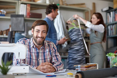 Buy stock photo Portrait of a young fashion designer sitting in the workshop while his colleagues work in the background