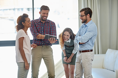 Buy stock photo Shot of a group of colleagues laughing while using a digital tablet together at work