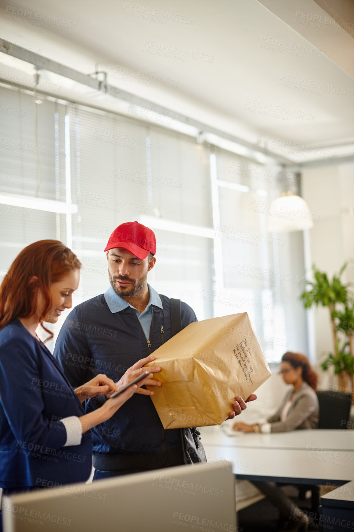 Buy stock photo Shot of a young woman receiving a package from a deliveryman at her office