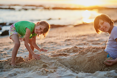 Buy stock photo Portrait of two young siblings playing together in the sand at the beach