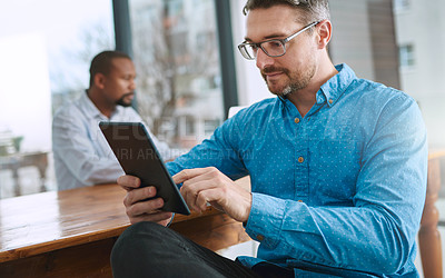 Buy stock photo Shot of a businessman using his tablet with a colleague in the background