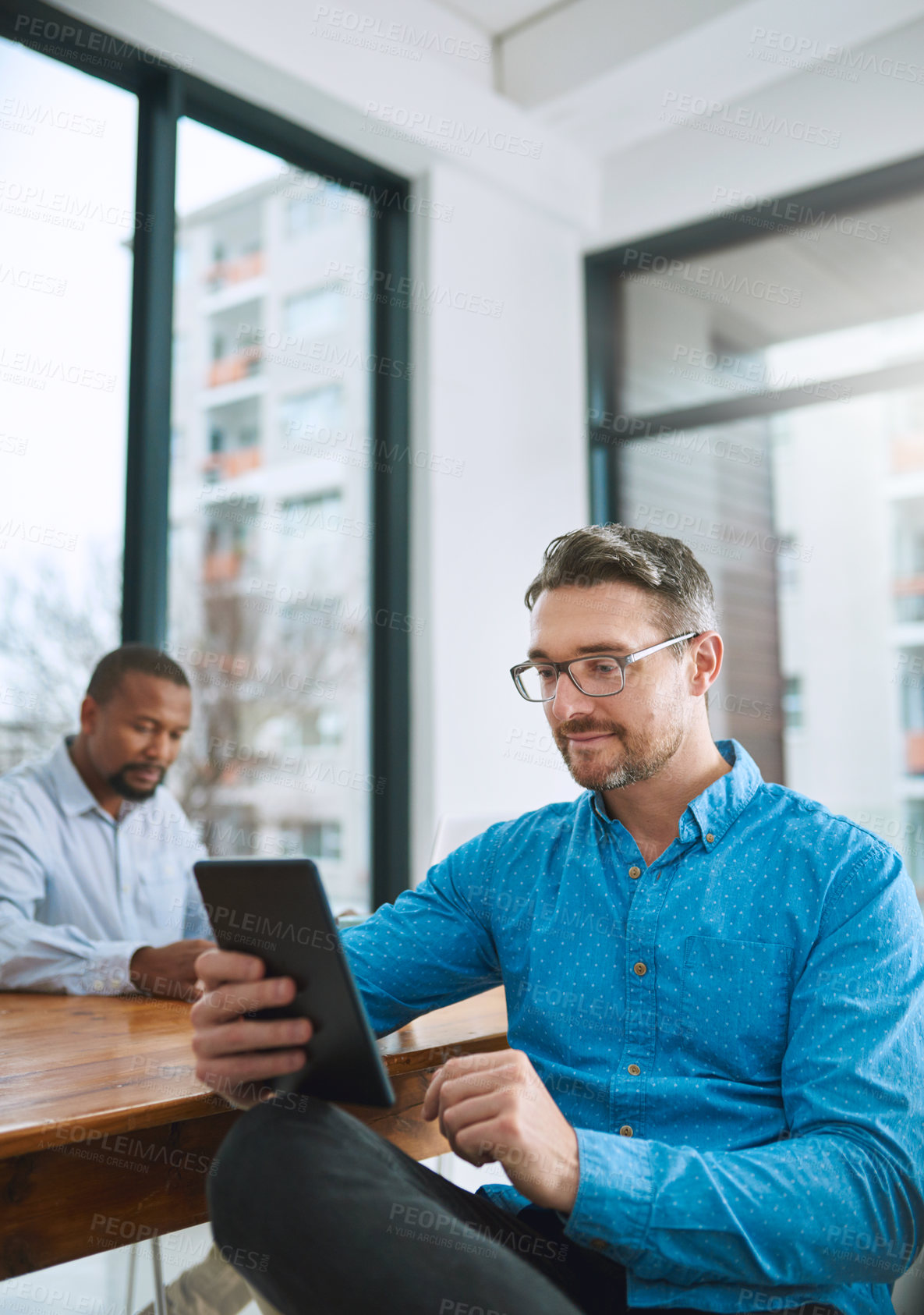 Buy stock photo Shot of a businessman using his tablet with a colleague in the background