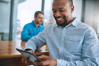 Buy stock photo Shot of a businessman using his tablet with a colleague in the background