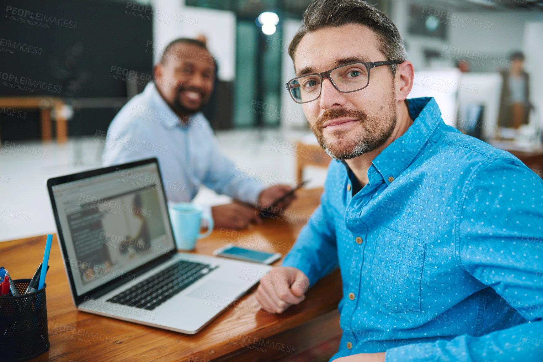 Buy stock photo Portrait of a businessman using his laptop with a colleague in the background