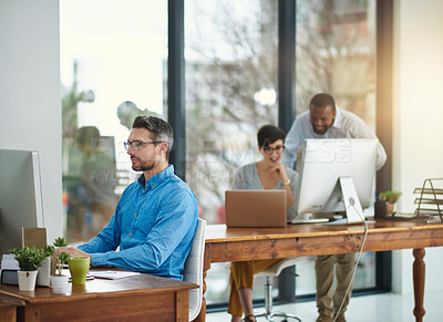 Buy stock photo Shot of a businessman working in the office with two colleagues in the background