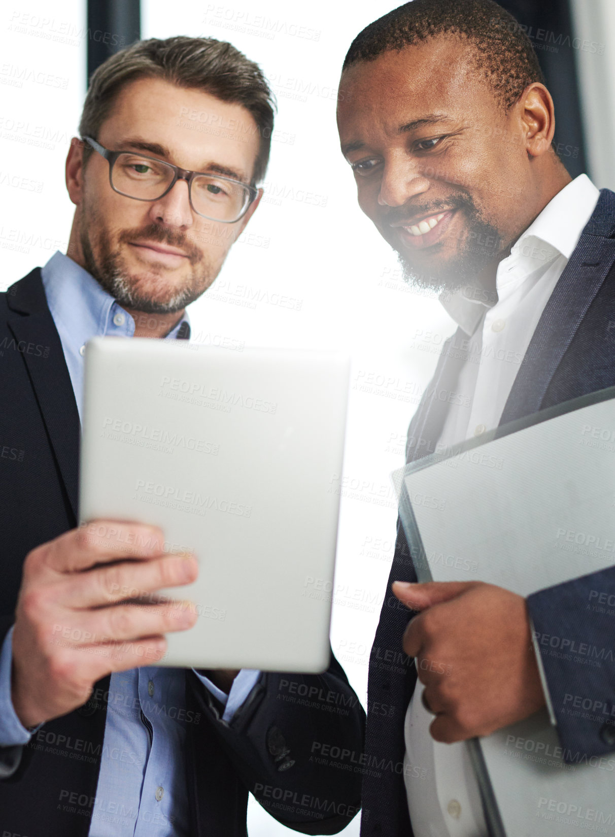 Buy stock photo Shot of two businessmen using a digital tablet together at work