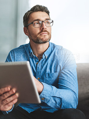 Buy stock photo Shot of a businessman using his digital tablet while sitting on a sofa in the office