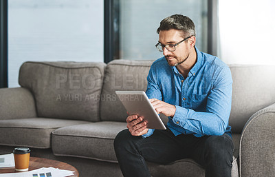 Buy stock photo Shot of a businessman using his digital tablet while sitting on a sofa in the office