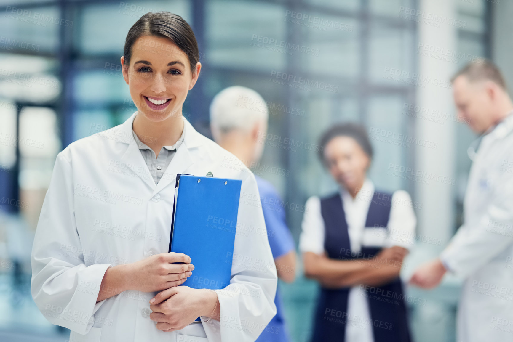 Buy stock photo Portrait of a young female doctor standing in a hospital with colleagues in the background