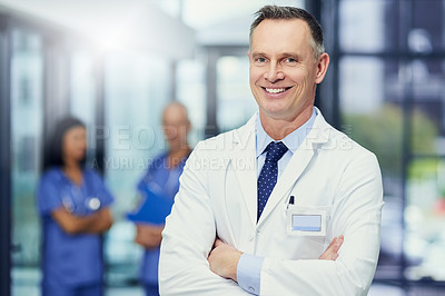 Buy stock photo Portrait of a mature male doctor standing in a hospital with colleagues in the background