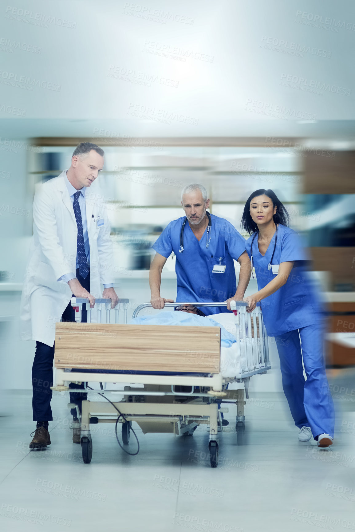 Buy stock photo Shot of a group of medical professionals rushing a patient on a gurney down a hospital corridor