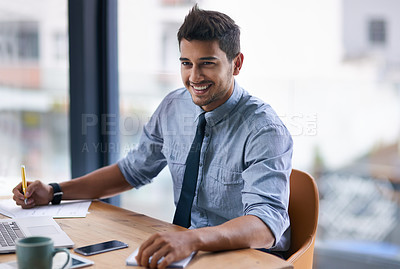 Buy stock photo Shot of a young businessman writing notes while working on a laptop in a modern office