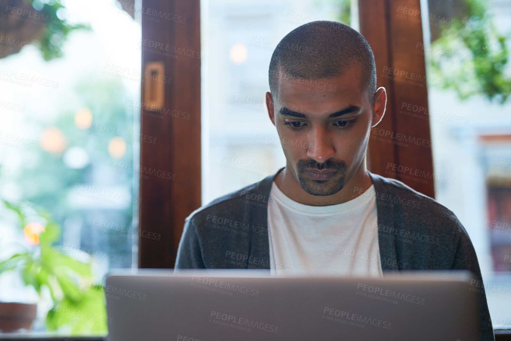 Buy stock photo Cropped shot of a young man working on his laptop in a coffee shop