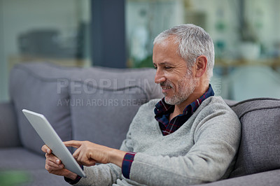 Buy stock photo Shot of a mature businessman using a digital tablet while sitting on a sofa in an office