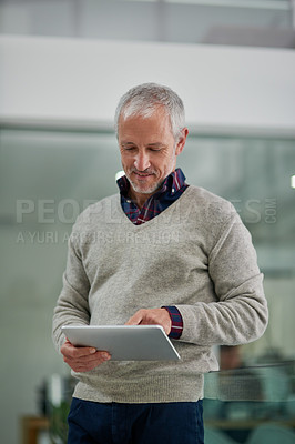 Buy stock photo Shot of a mature businessman using a digital tablet while standing in an office