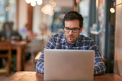 Buy stock photo Shot of a young man using his laptop while sitting in a coffee shop