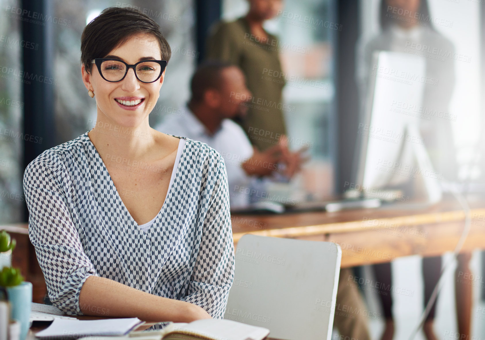 Buy stock photo Portrait of a young businesswoman sitting at her desk with colleagues in the background