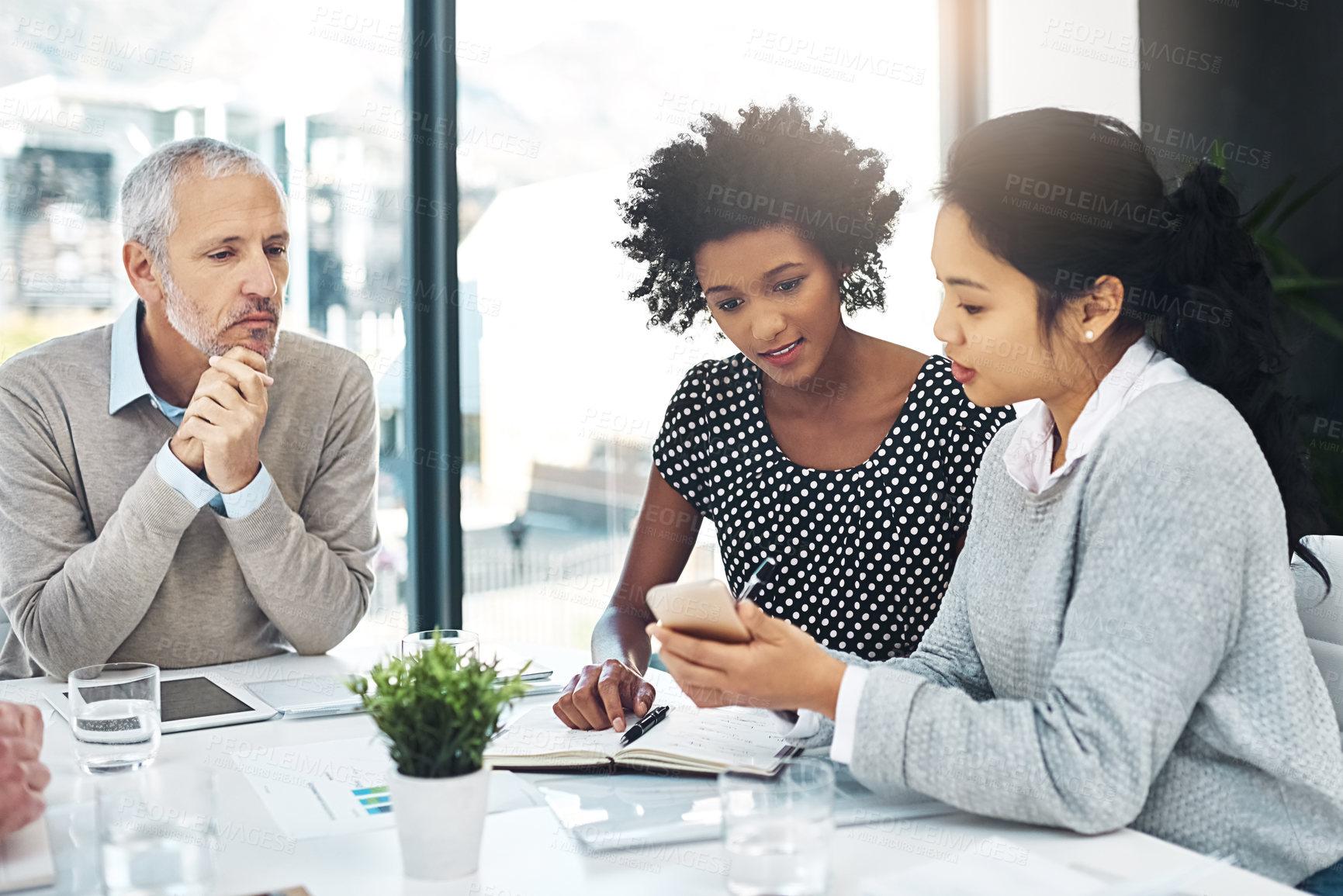 Buy stock photo Shot of a group of coworkers talking together over a cellphone while sitting at a table in an office