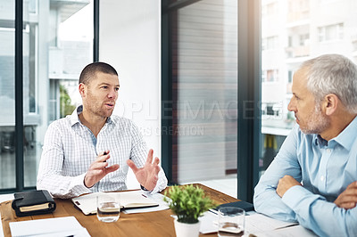 Buy stock photo Shot of a businessman gesturing while talking with a coworker in an office boardroom