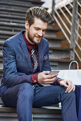 Buy stock photo Shot of a well dressed young man using his phone on a shopping spree
