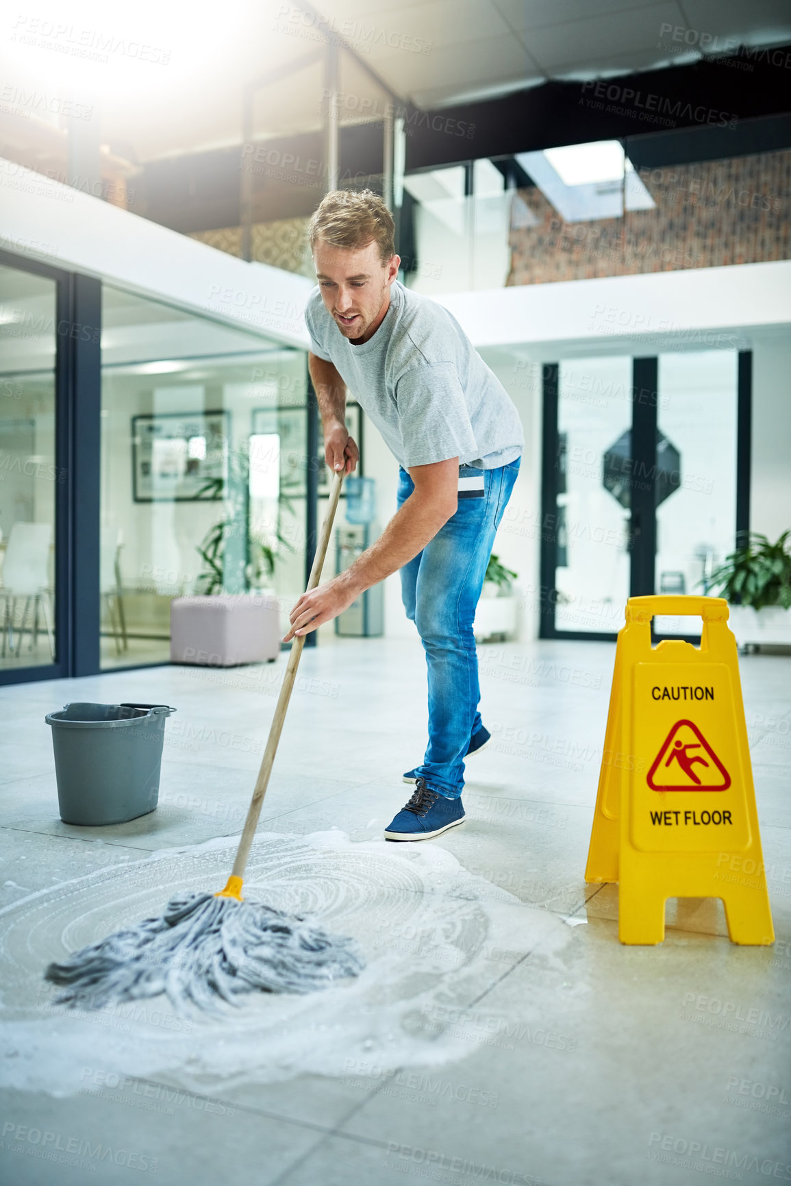 Buy stock photo Shot of a young man mopping the office floor