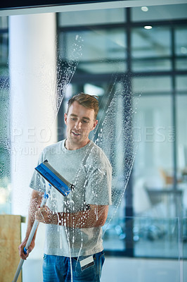 Buy stock photo Shot of a young man cleaning the windows in the office