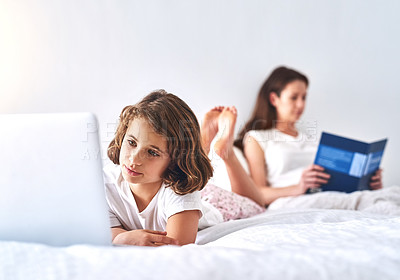 Buy stock photo Cropped shot of a young girl using a laptop while her mom reads a book in the background