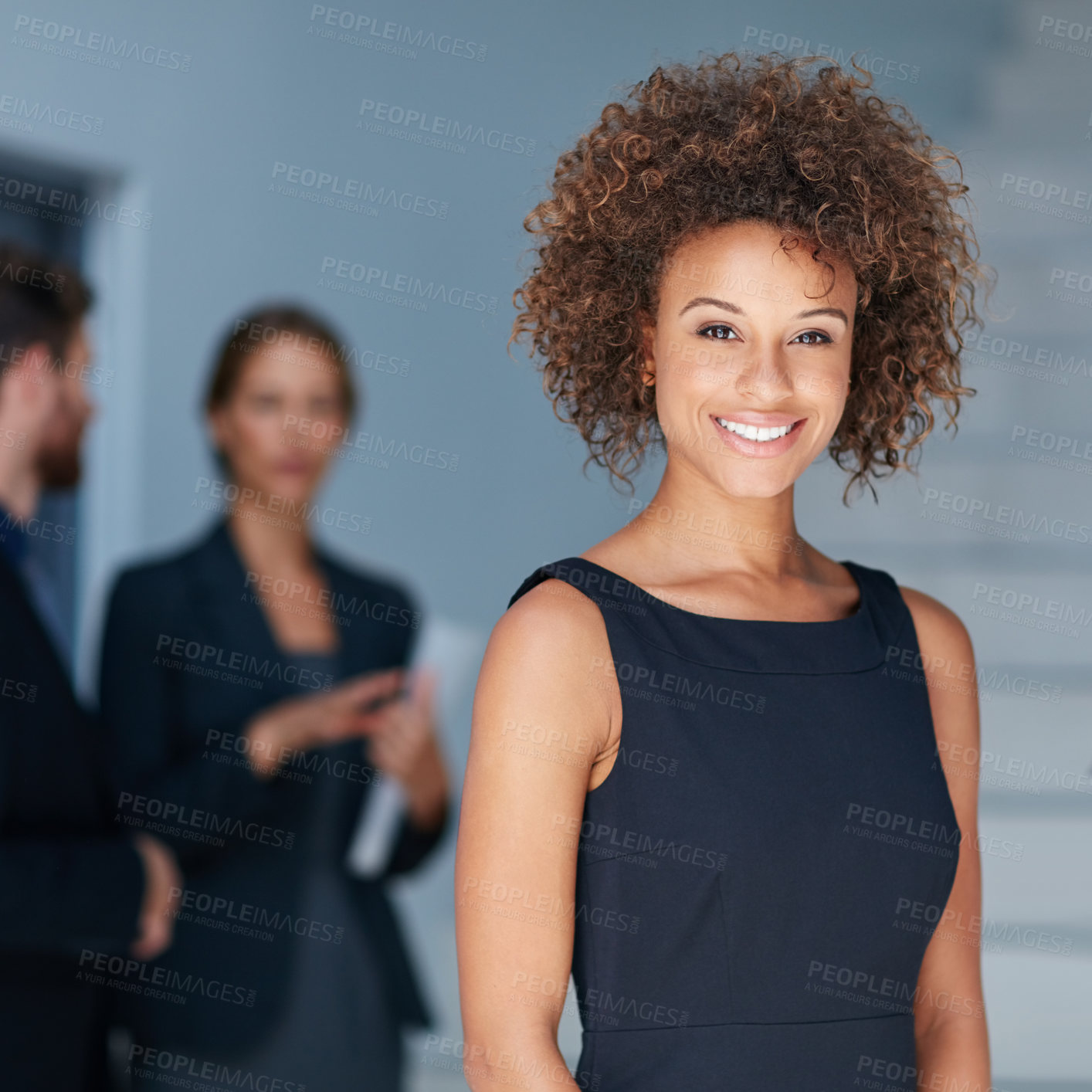 Buy stock photo Portrait of a young businesswoman standing in an office with colleagues in the background