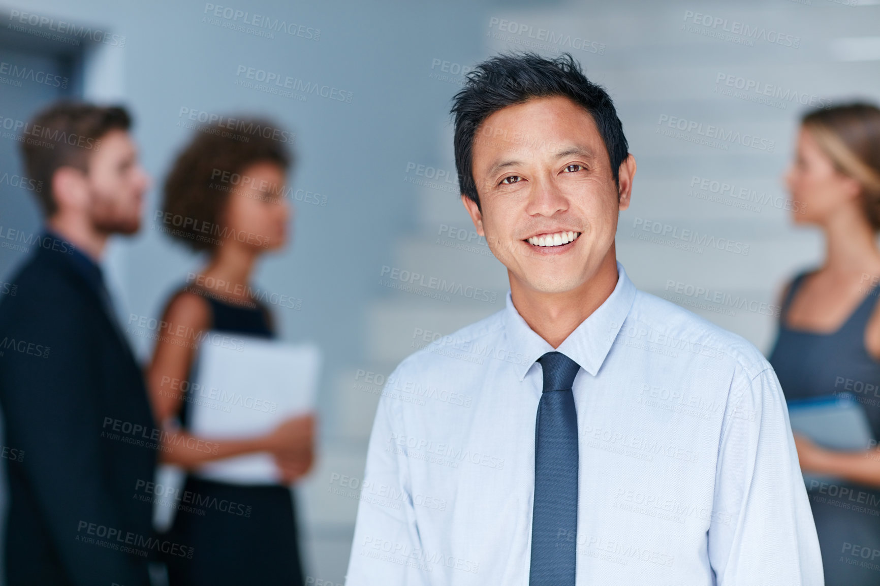 Buy stock photo Portrait of a young businessman standing in an office with colleagues in the background