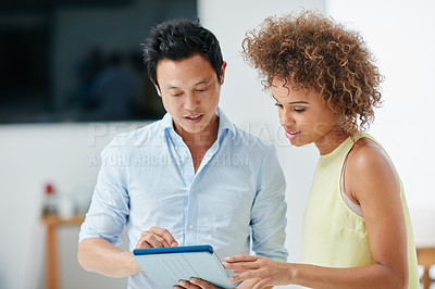 Buy stock photo Shot of a businessman and his female colleague looking at something together on a tablet in the office