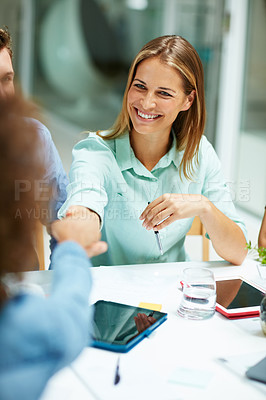 Buy stock photo Shot of two businesspeople shaking hands together at a table in an office while colleagues look on
