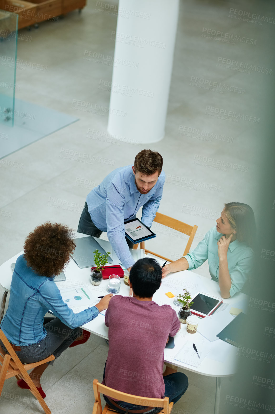 Buy stock photo High angle shot of two businesspeople shaking hands together at a table in an office while colleagues look on