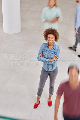 Buy stock photo High angle portrait of a young businesswoman standing in an office with colleagues walking around her