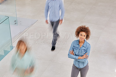 Buy stock photo High angle portrait of a young businesswoman standing in an office with colleagues walking around her