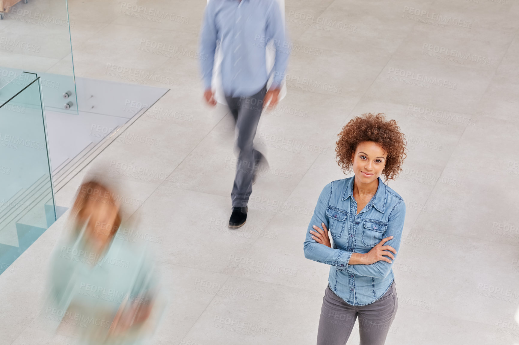 Buy stock photo High angle portrait of a young businesswoman standing in an office with colleagues walking around her