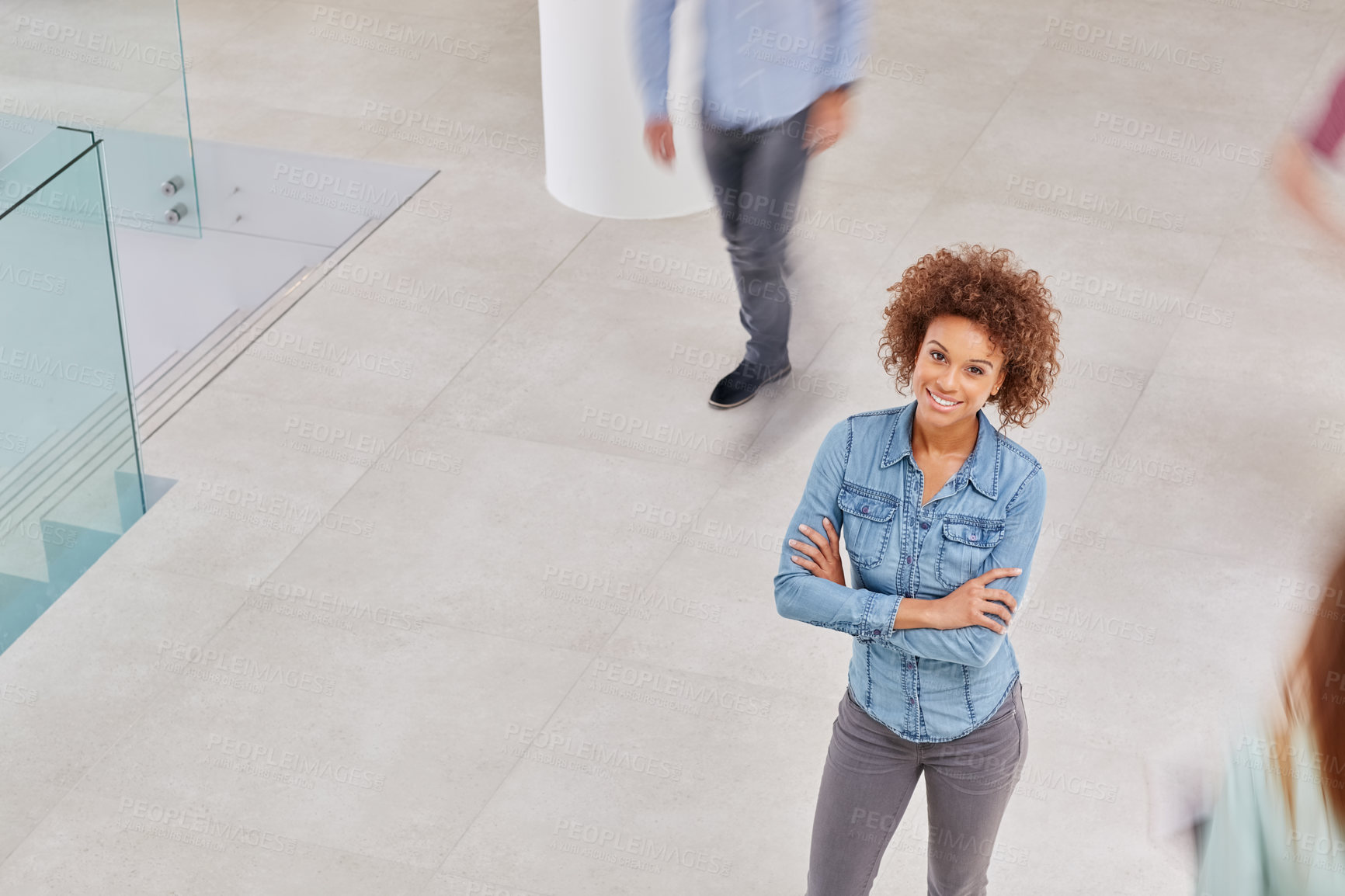 Buy stock photo High angle portrait of a young businesswoman standing in an office with colleagues walking around her