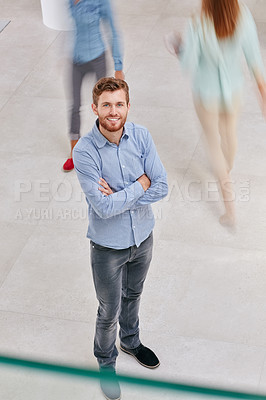 Buy stock photo High angle portrait of a young businessman standing in an office with colleagues walking around him