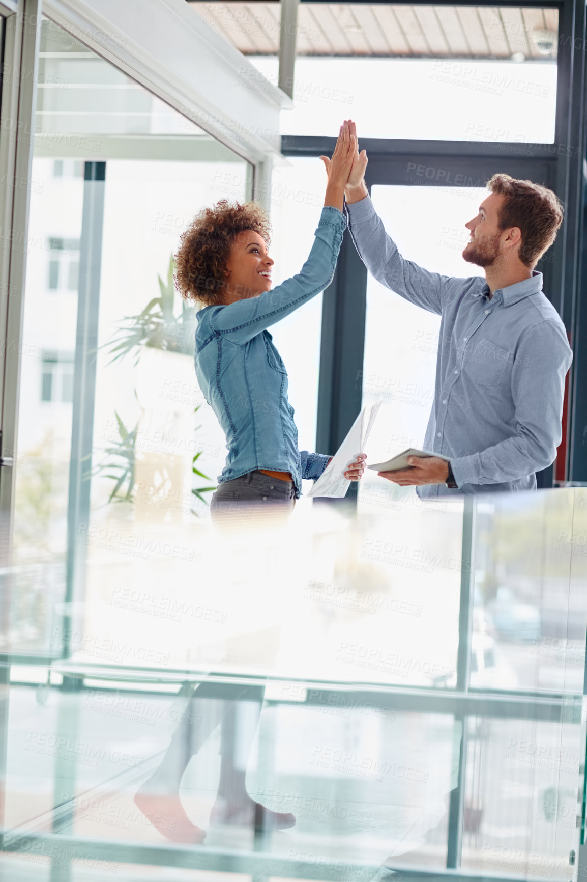 Buy stock photo Shot of two colleagues high fiving each other in an office