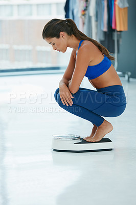Buy stock photo Shot of a fit young woman weighing herself on a scale