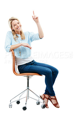 Buy stock photo Studio portrait of a happy young woman sitting on a chair pointing at copyspace against a white background