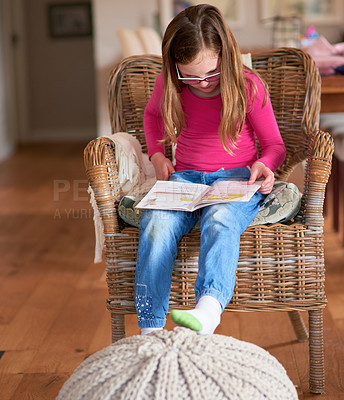 Buy stock photo Shot of a little girl reading a book on her own at home