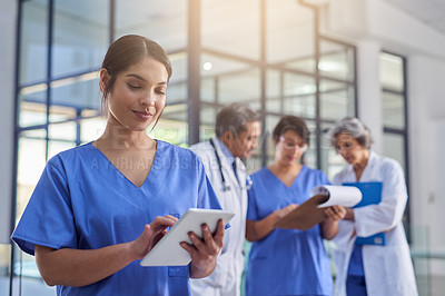 Buy stock photo Cropped shot of a medical practitioner looking at a patient's file on a digital tablet with colleagues in the background